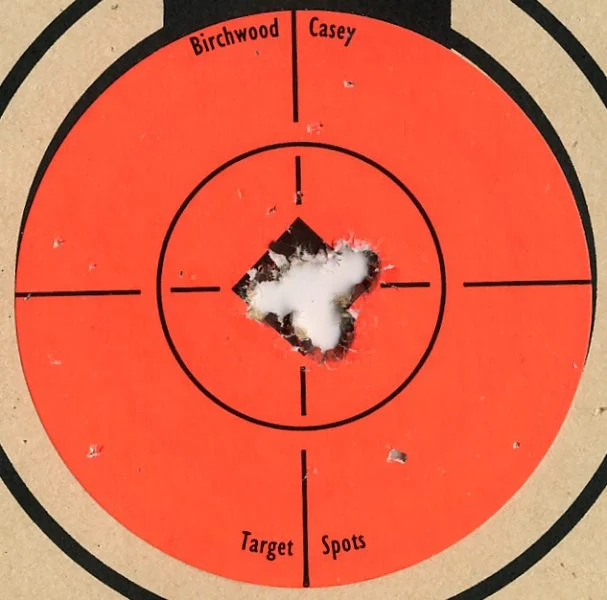 An orange target with bullet holes in the middle in a tight group.