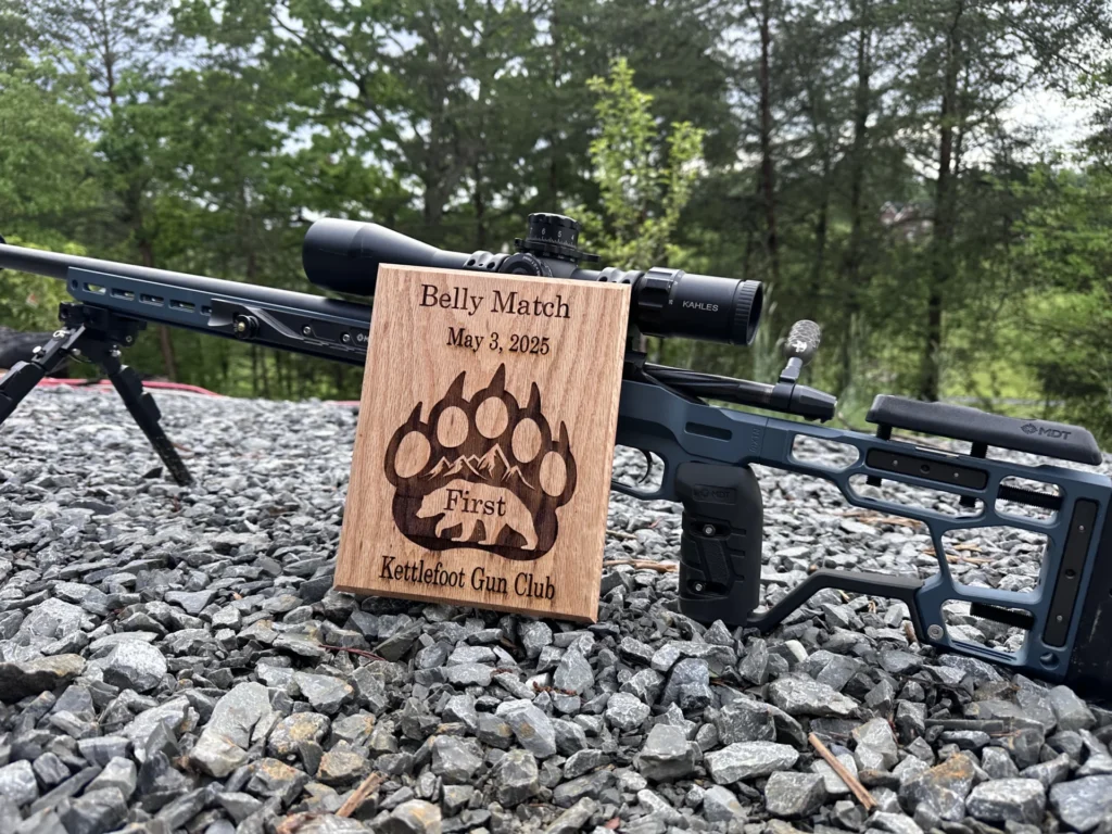 A custom built rifle with a bipod sitting on gravel.